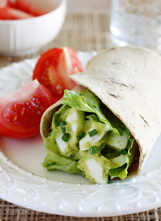 Avocado Egg Salad wrapped in a tortilla with fresh chopped tomatoes pictured in the background