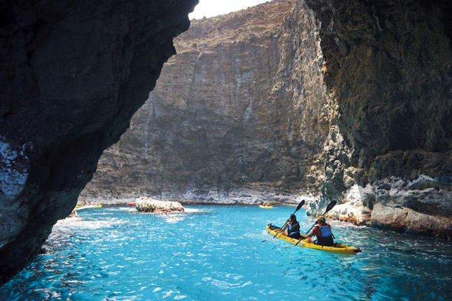 Hawaii, Kauai, Na Pali Coast, Kayakers exploring sea cave along coastline, Waterfall from cliffside. Editorial Use Only.