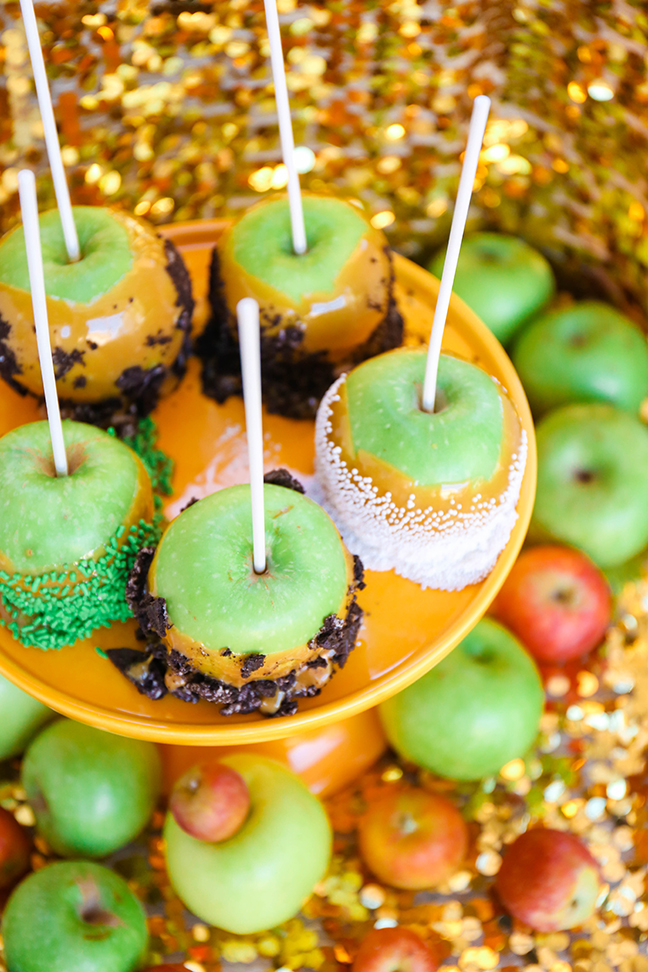 caramel apples dipped in candy on yellow cake stand