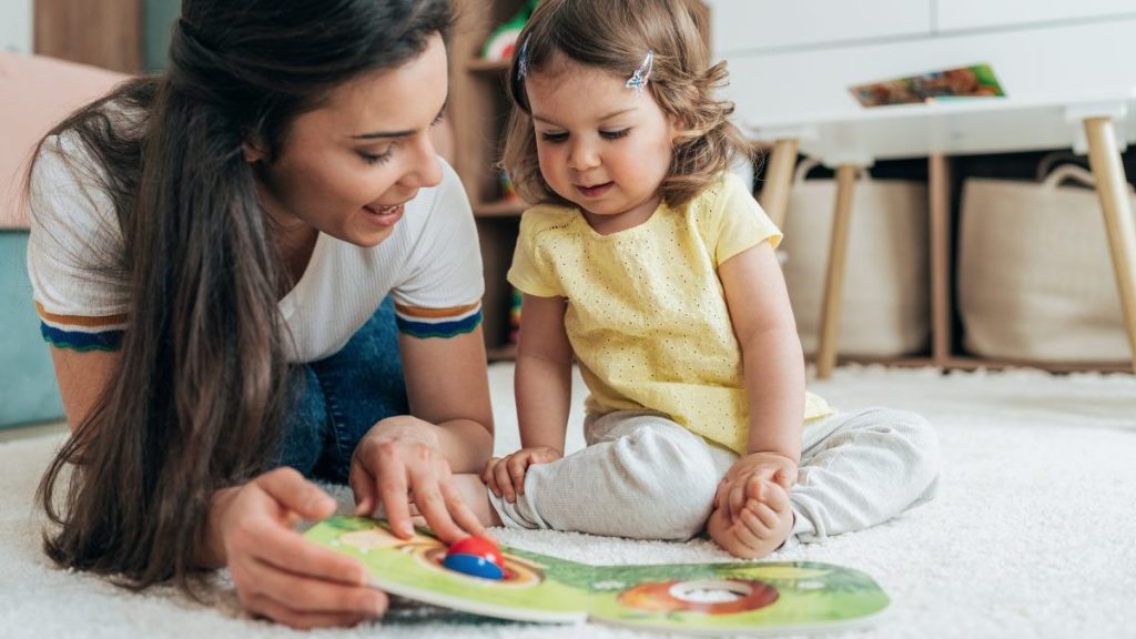 Young beautiful mother reading book with toddler daughter on the floor at home